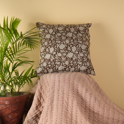 Decorative pillow with floral pattern on a bed next to a potted plant against a beige wall.