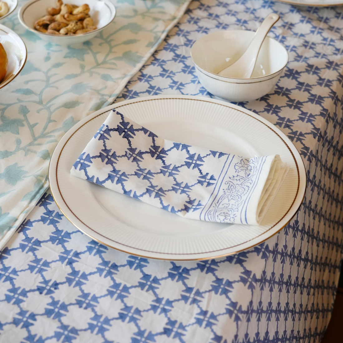 Table setting with a plate, folded napkin, and bowl with spoon on a patterned tablecloth.