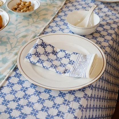 Table setting with a plate, folded napkin, and bowl with spoon on a patterned tablecloth.
