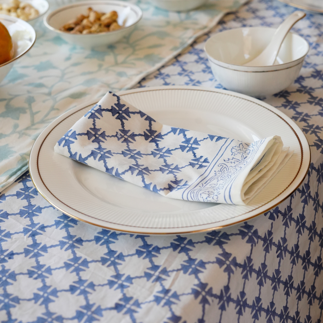 Table setting with a patterned blue and white napkin on a plate, placed on a tablecloth with a geometric design.