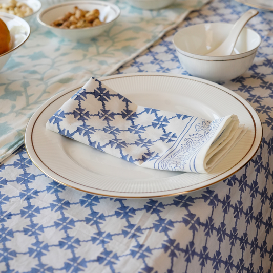 Table setting with a patterned blue and white napkin on a plate, placed on a tablecloth with a geometric design.