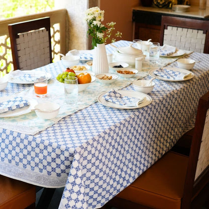 Dining table styled with a blue and white checkered tablecloth, table runner, napkins, plates, bowls, and cutlery.