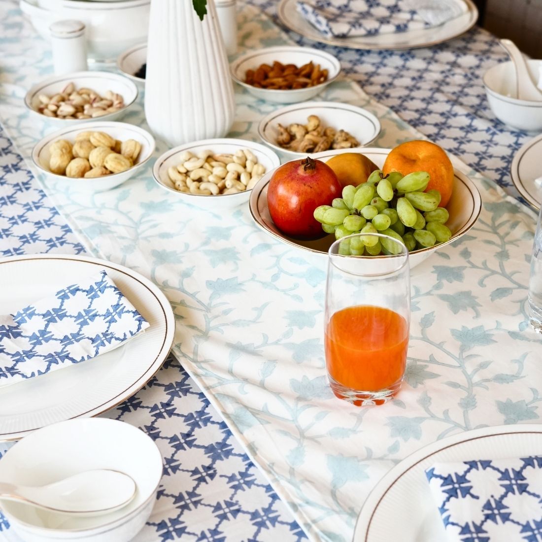 Table setting with fruit, nuts, and a glass of juice on a patterned tablecloth, table runner and napkins