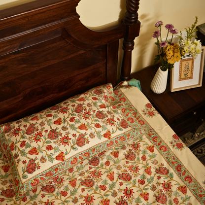 Floral-patterned bedspread on a bed with wooden headboard and side table with flowers.