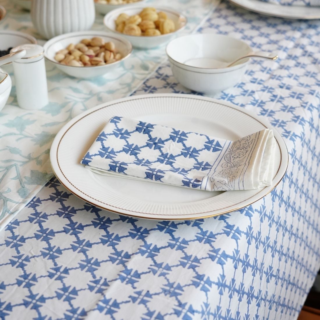 Dinner setting with blue and white patterned tablecloth, plates, and folded napkins.