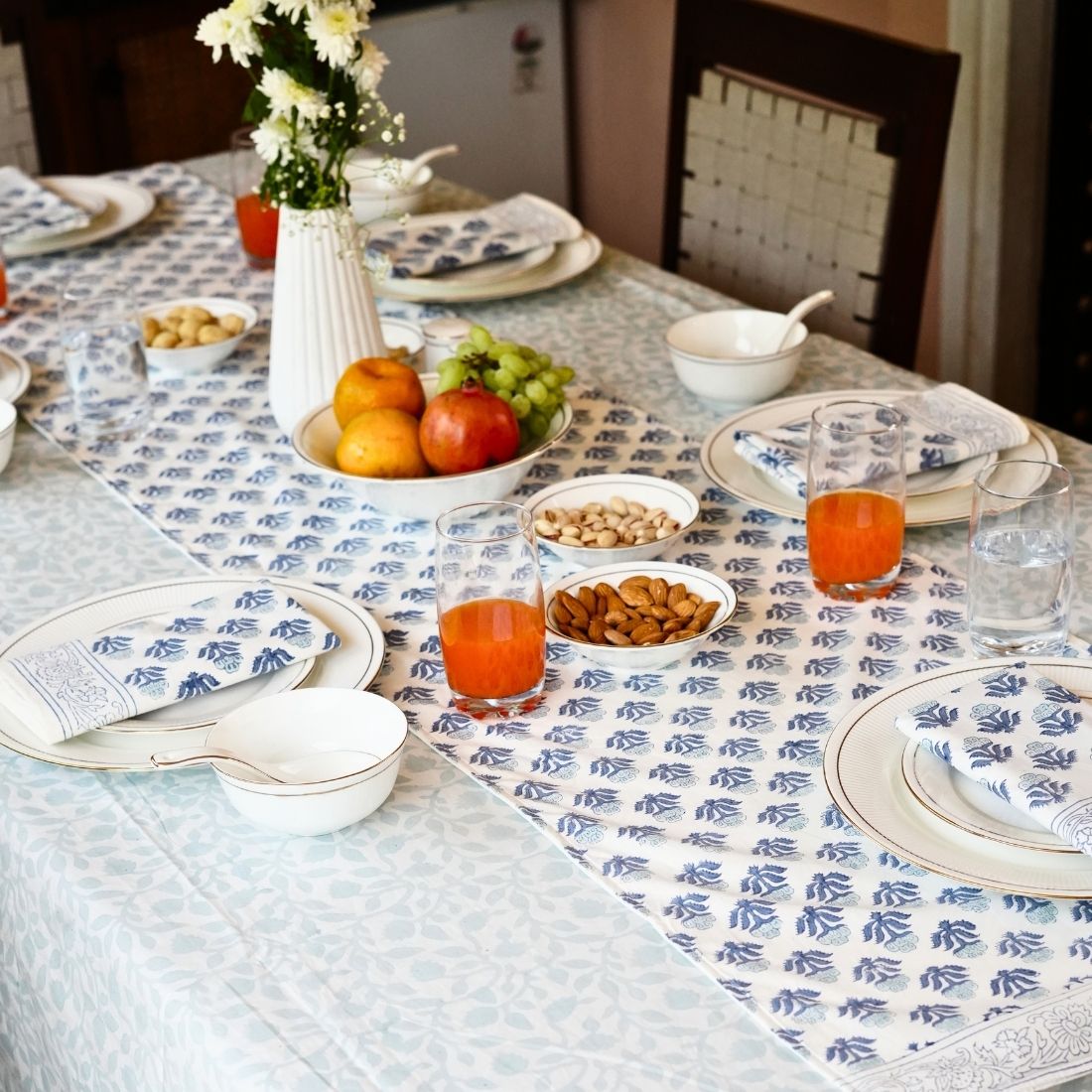 Dining table styled with a blue and white patterned tablecloth, table runner, napkins, plates, bowls, and cutlery.