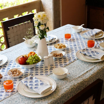 Dining table set with plates, glasses, and a vase of flowers on a patterned tablecloth, table runner and napkins