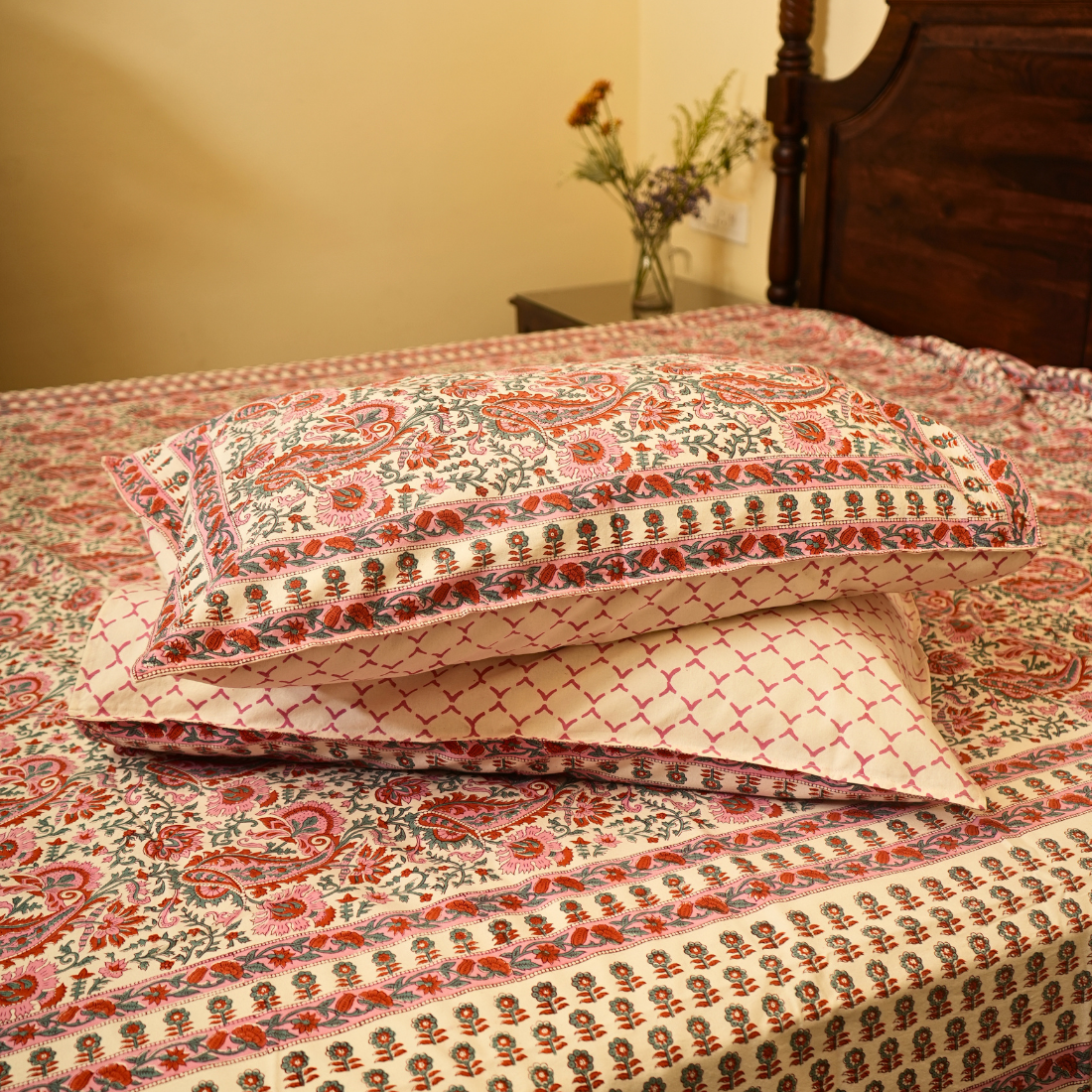 Patterned pillows on a bed with a wooden headboard and side table in the background.