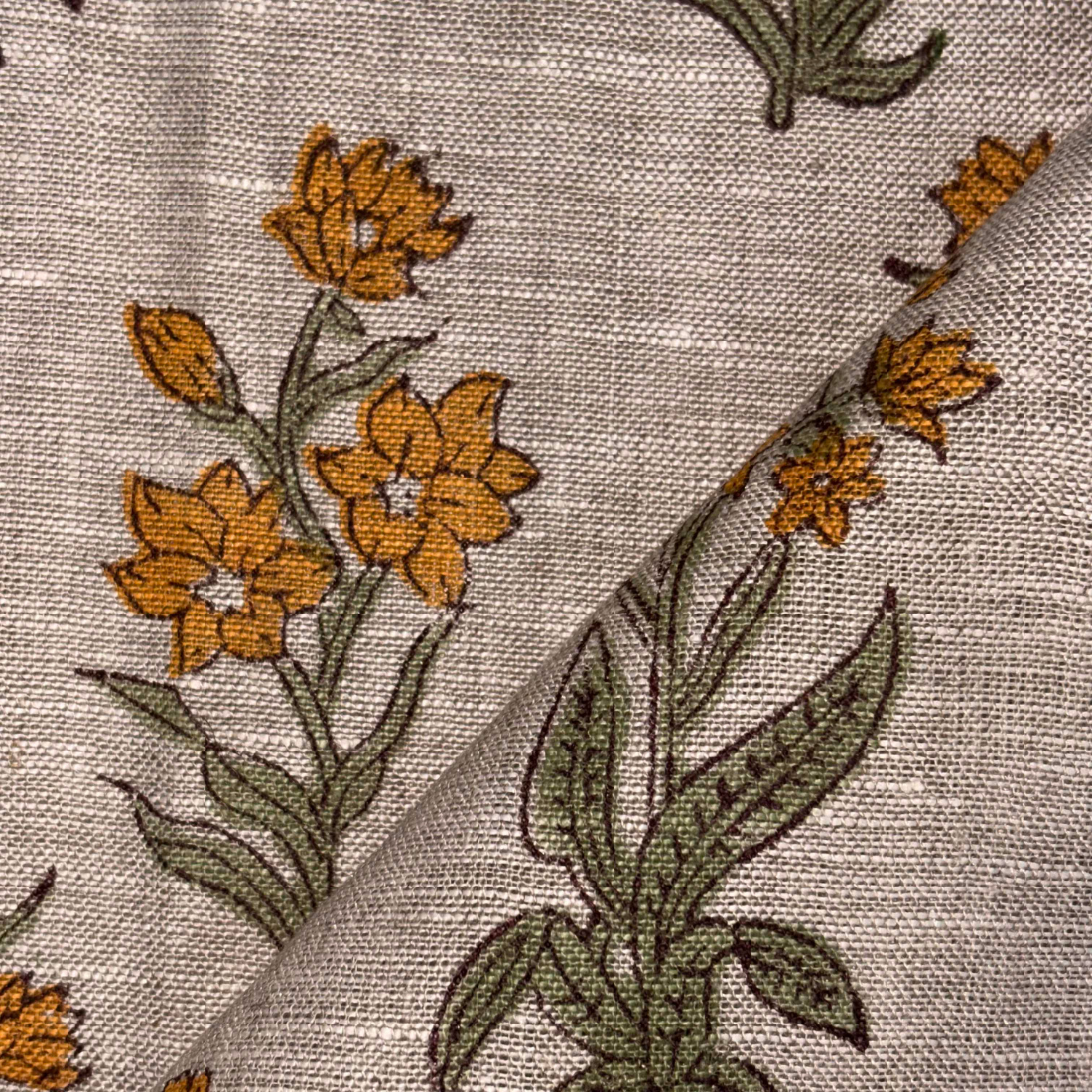Close-up of floral embroidery on fabric with brown flowers and green leaves.