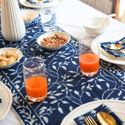 Table runner with orange juice, almonds, and patterned tablecloth.