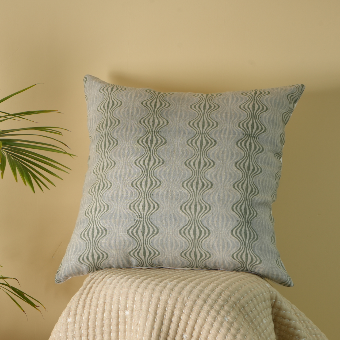 Decorative pillow with wavy pattern on a beige surface against a beige wall.