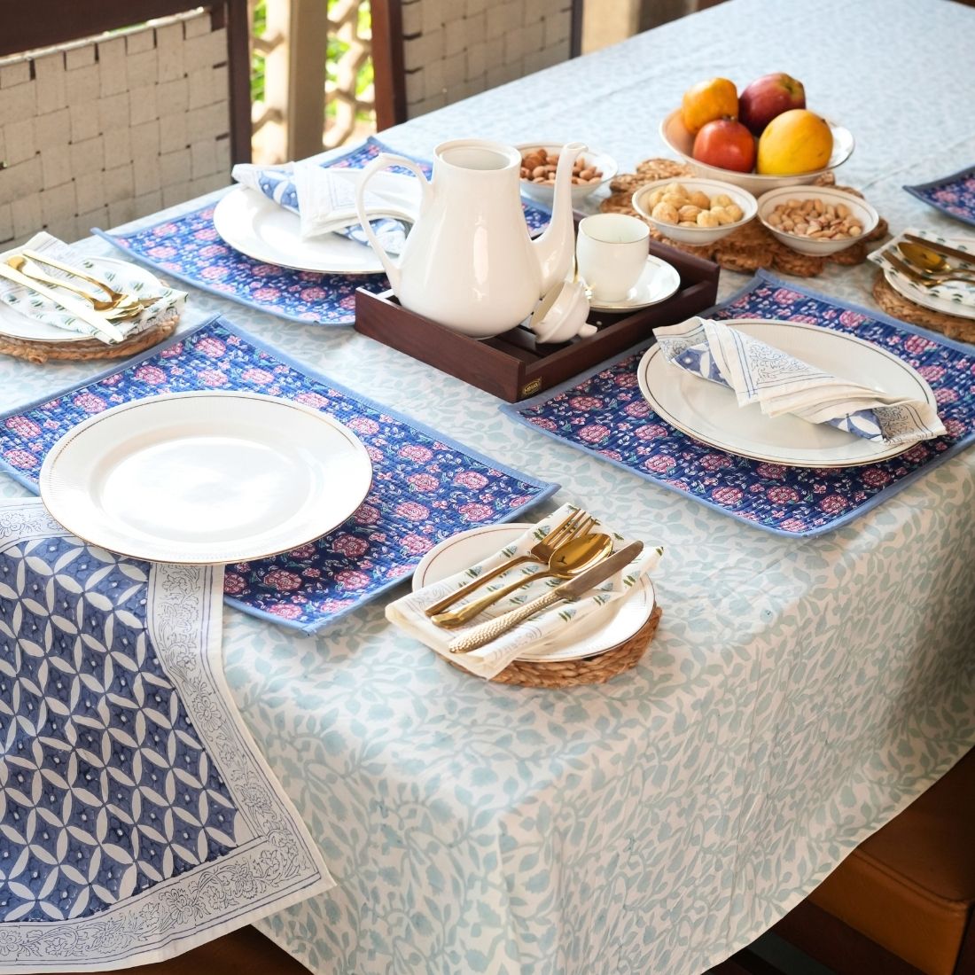 Dining table set with plates, cutlery, and a fruit bowl on a patterned table runner and placemats