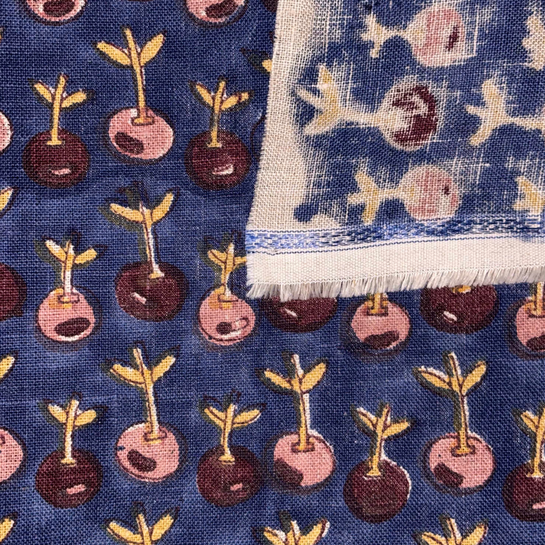 Close-up of a fabric with a pattern of plants and seeds on a blue background.