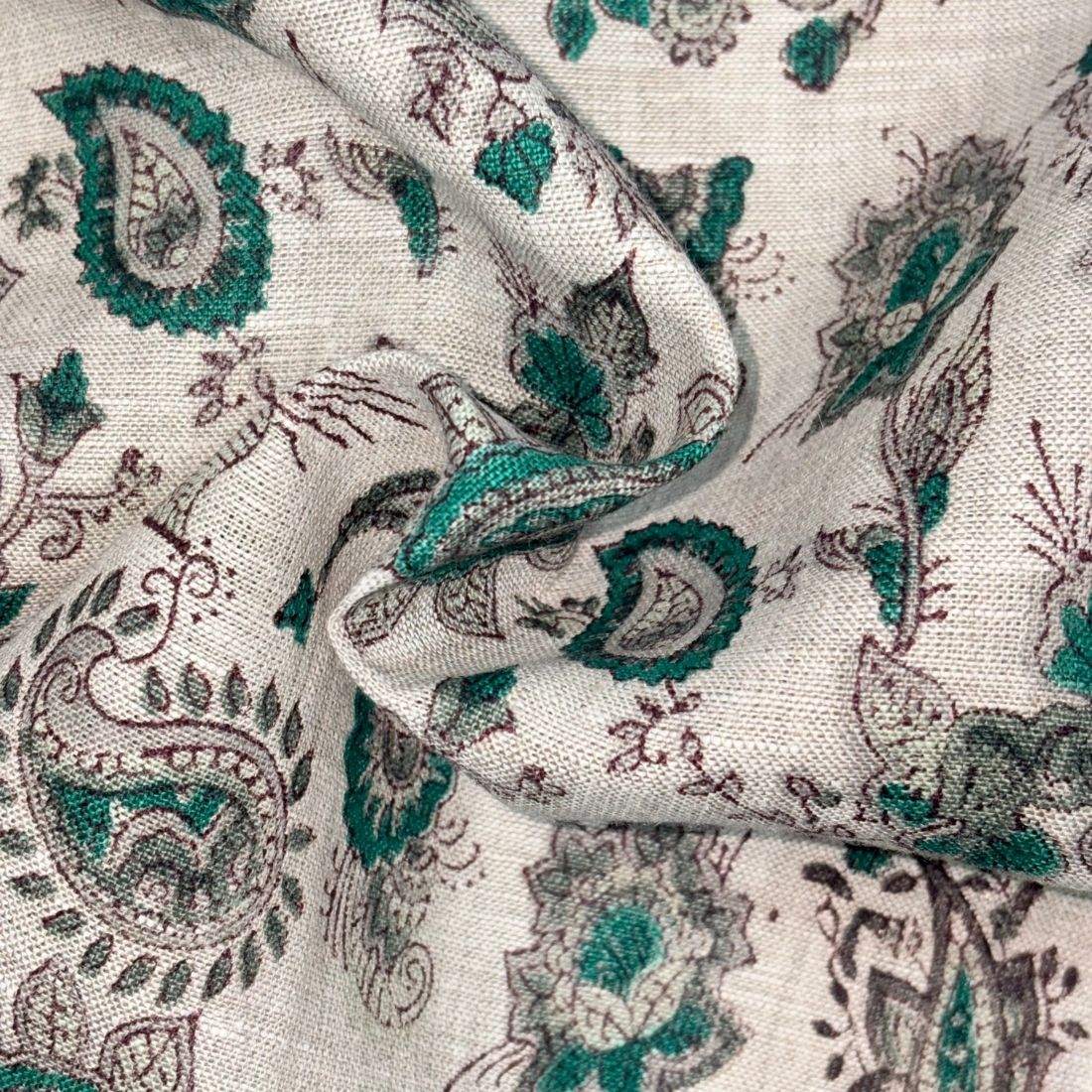 Close-up of fabric with green and brown paisley pattern on a grey background