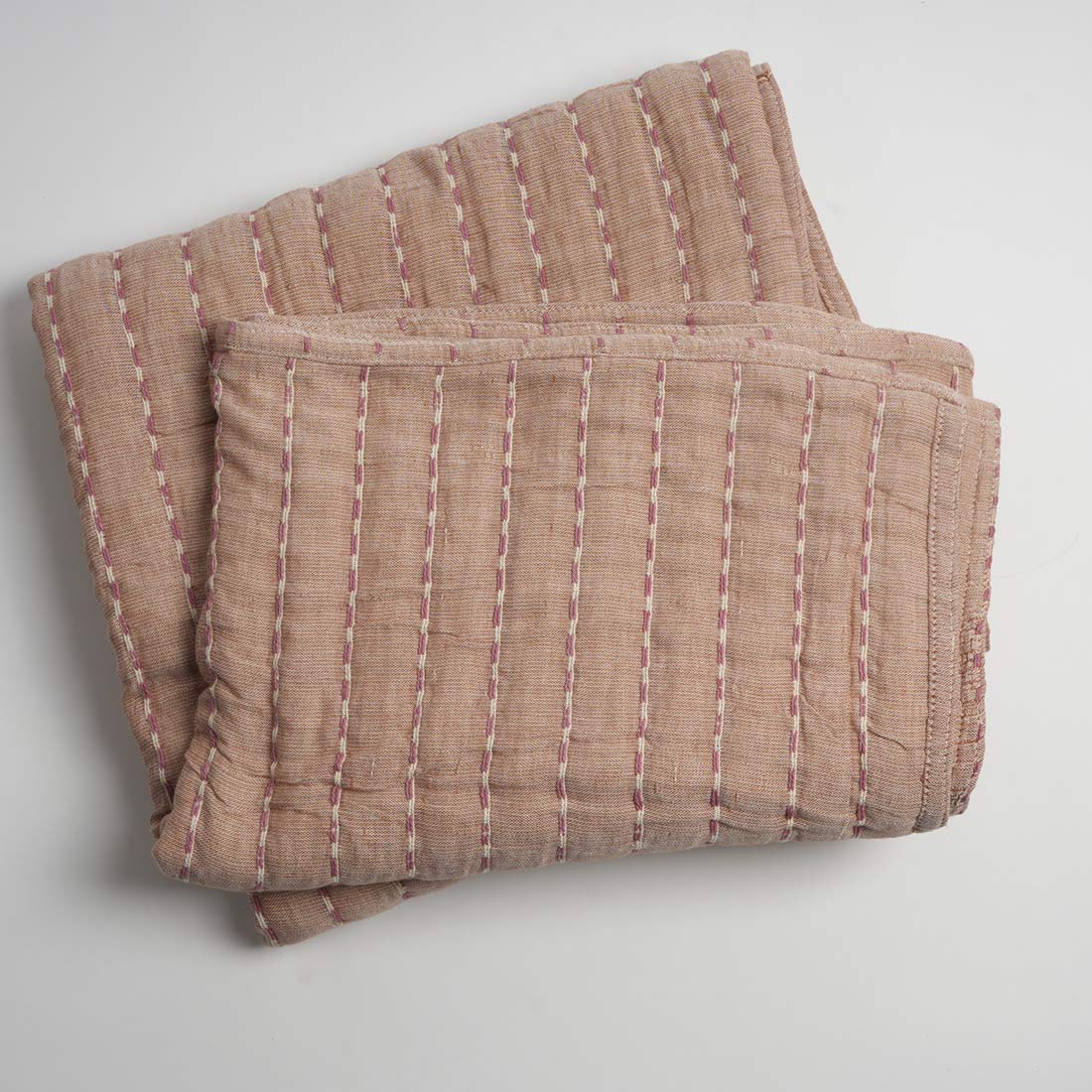 Folded brown quilt with white stitching on a light gray background