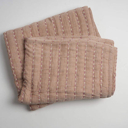 Folded brown quilt with white stitching on a light gray background