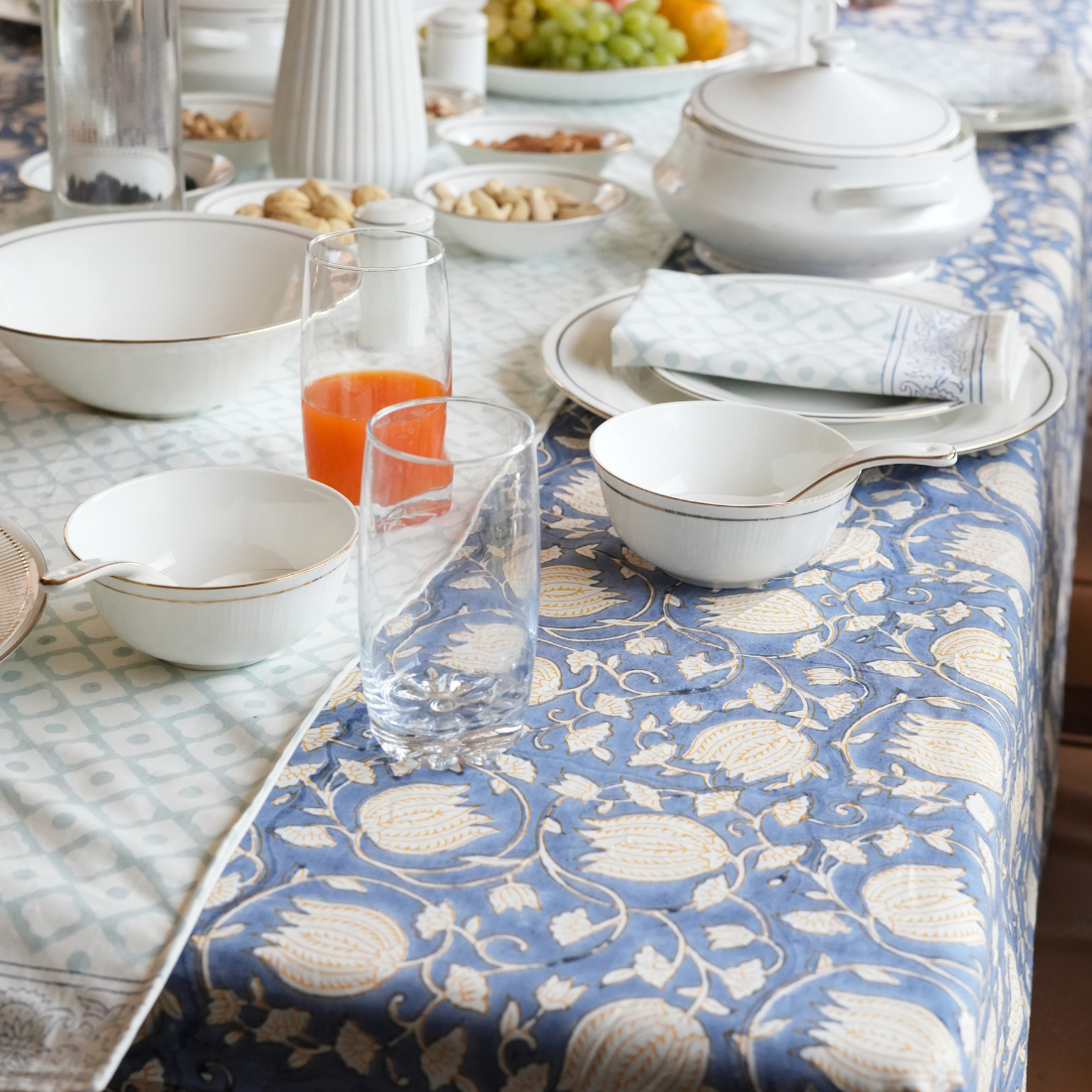 Dining table with floral-patterned table linen set with white dishes and glasses.