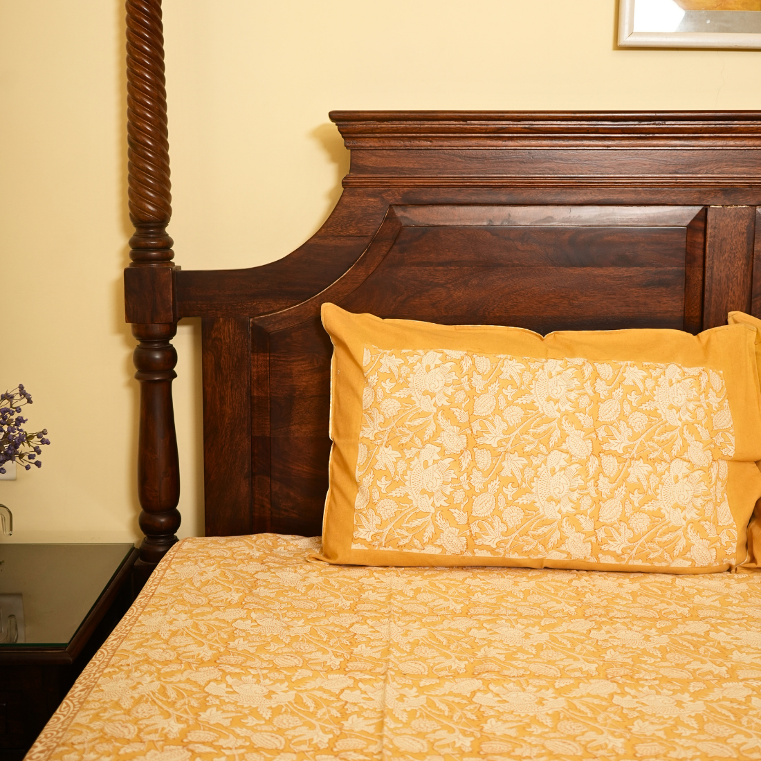 Bed with wooden headboard and yellow floral bedding in a room.