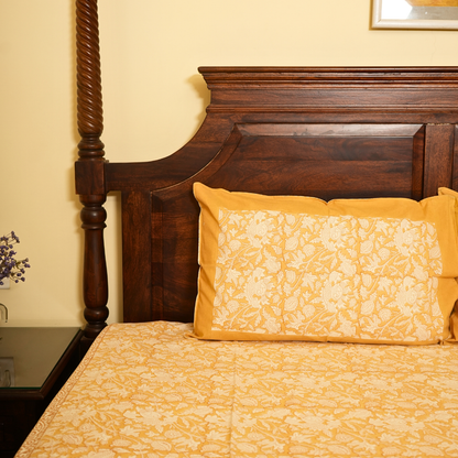 Bed with wooden headboard and yellow floral bedding in a room.