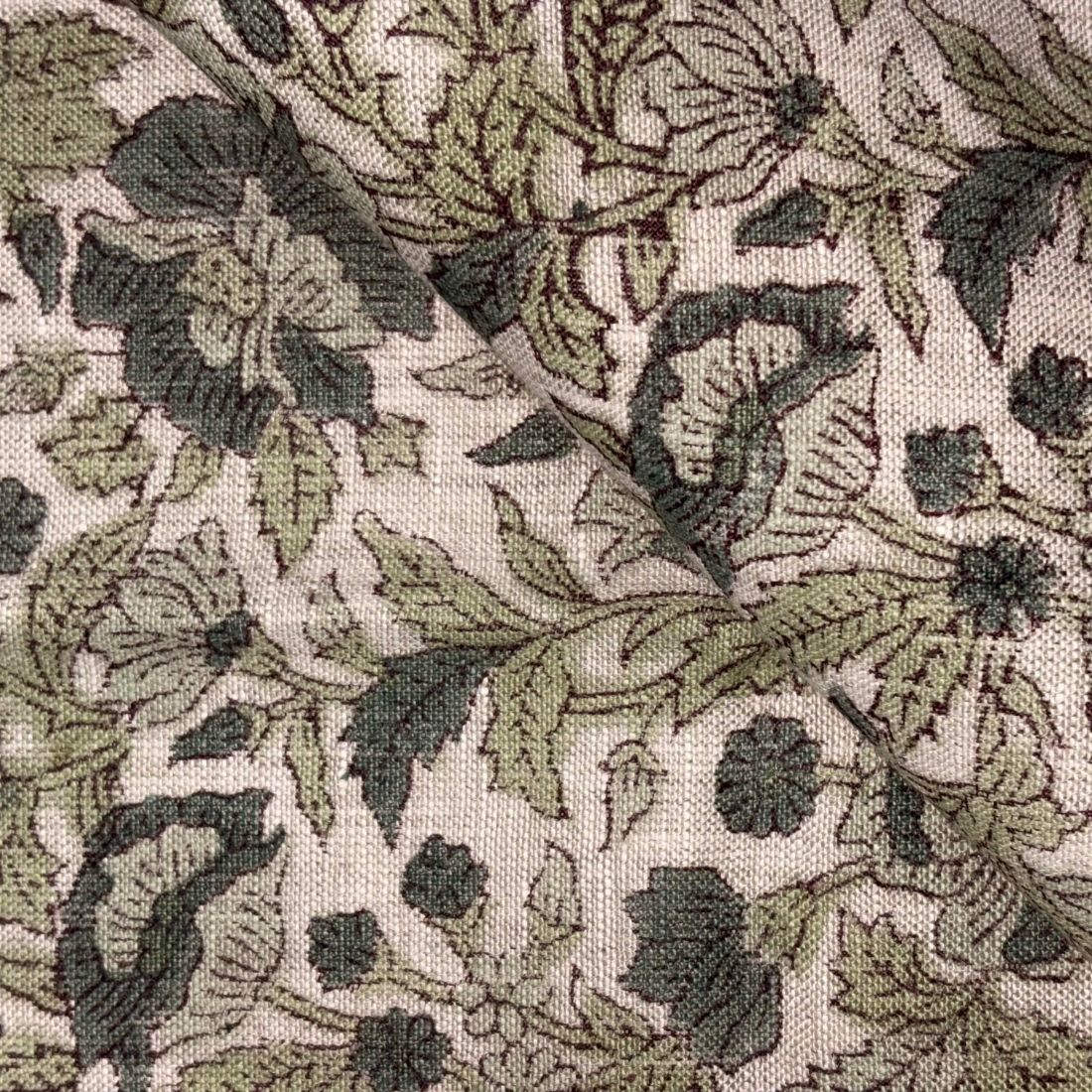 Close-up of a floral patterned fabric with green and black leaves on a beige background