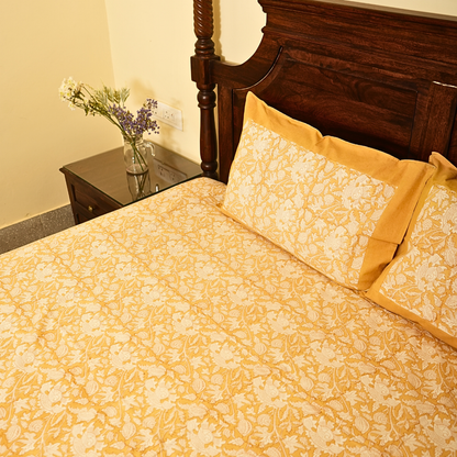Bed with yellow floral bedding and wooden headboard in a room.