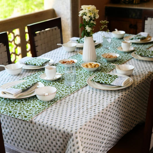 Dining table styled with a green and white tablecloth, table runner, napkins, plates, bowls, and cutlery.