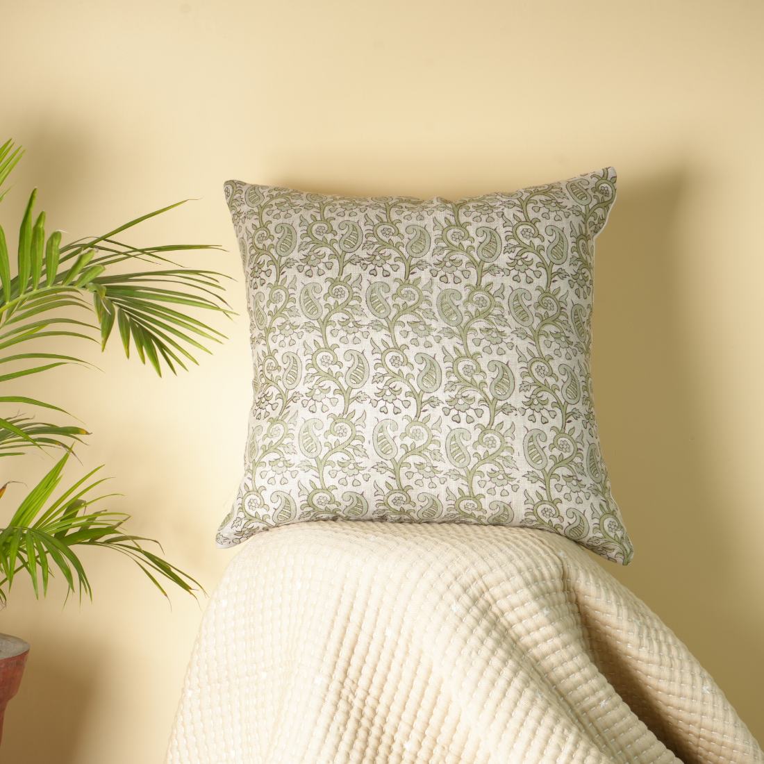 Decorative pillow with floral pattern on a surface against a beige wall with a plant.