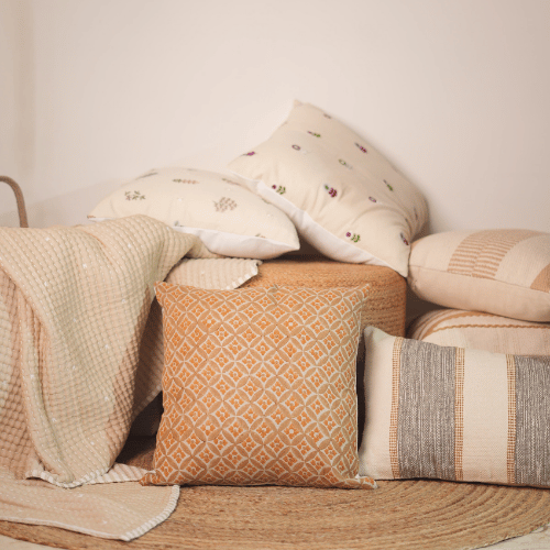 Collection of patterned pillows and a blanket on a wooden surface with a neutral background