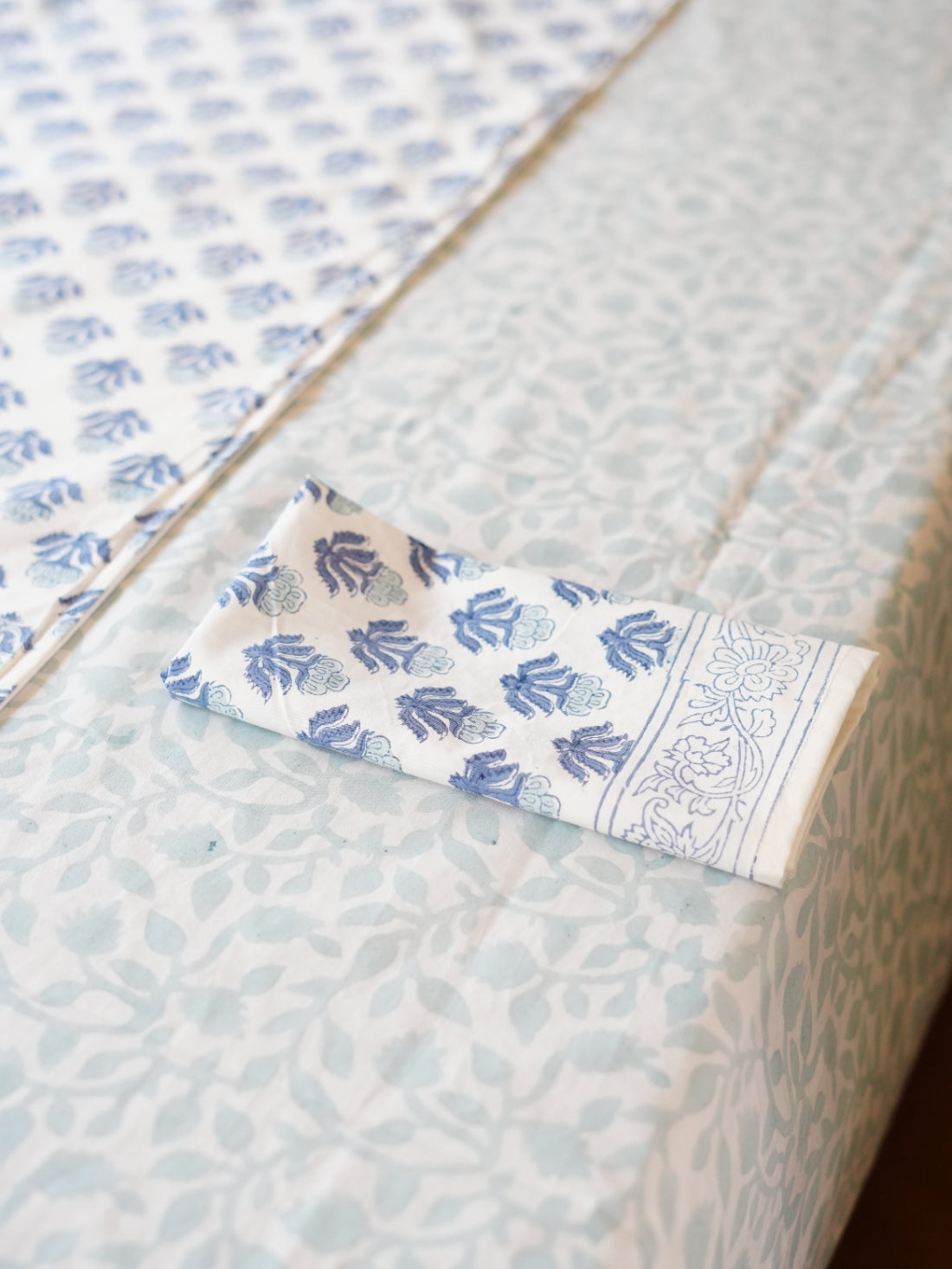 Close-up of a napkin with blue floral patterns on patterned tablecloth along with floral table runner