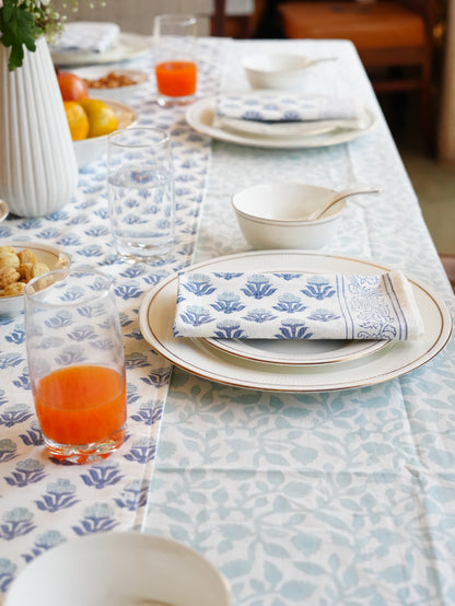 Dining table set with blue and white patterned tablecloth, floral patterned table runner and napkin