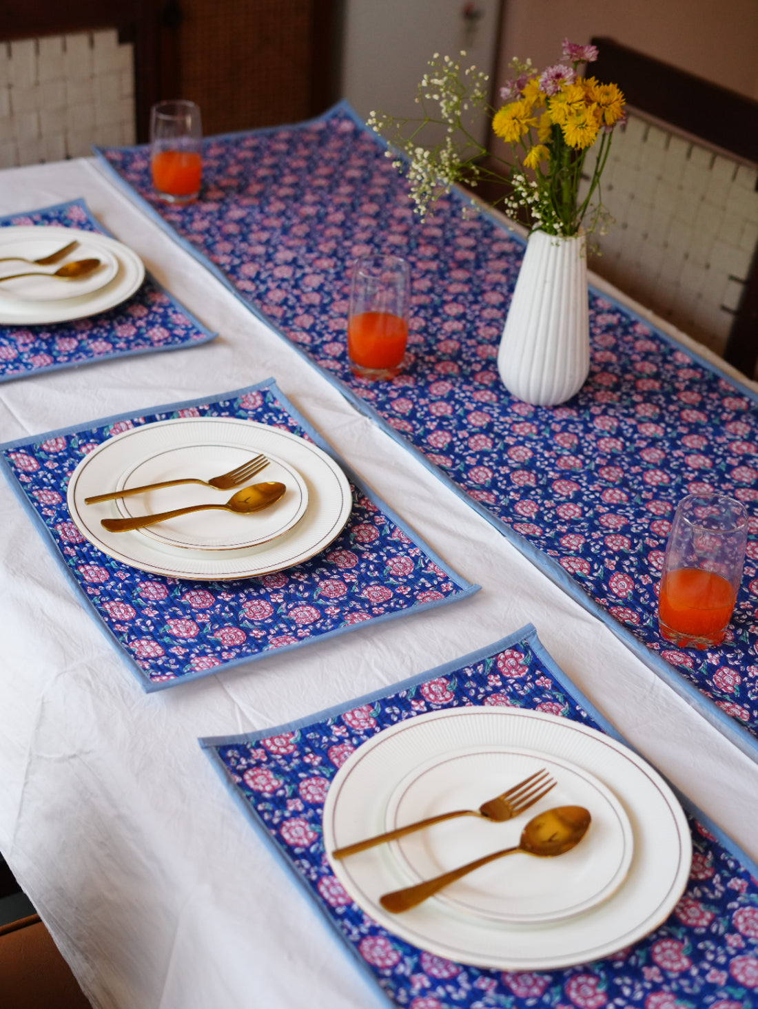 Table setting with floral table runner, placemats, plates, and cutlery.