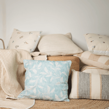 Collection of pillows and a blanket on a sofa with a light blue pillow featuring a leaf pattern.