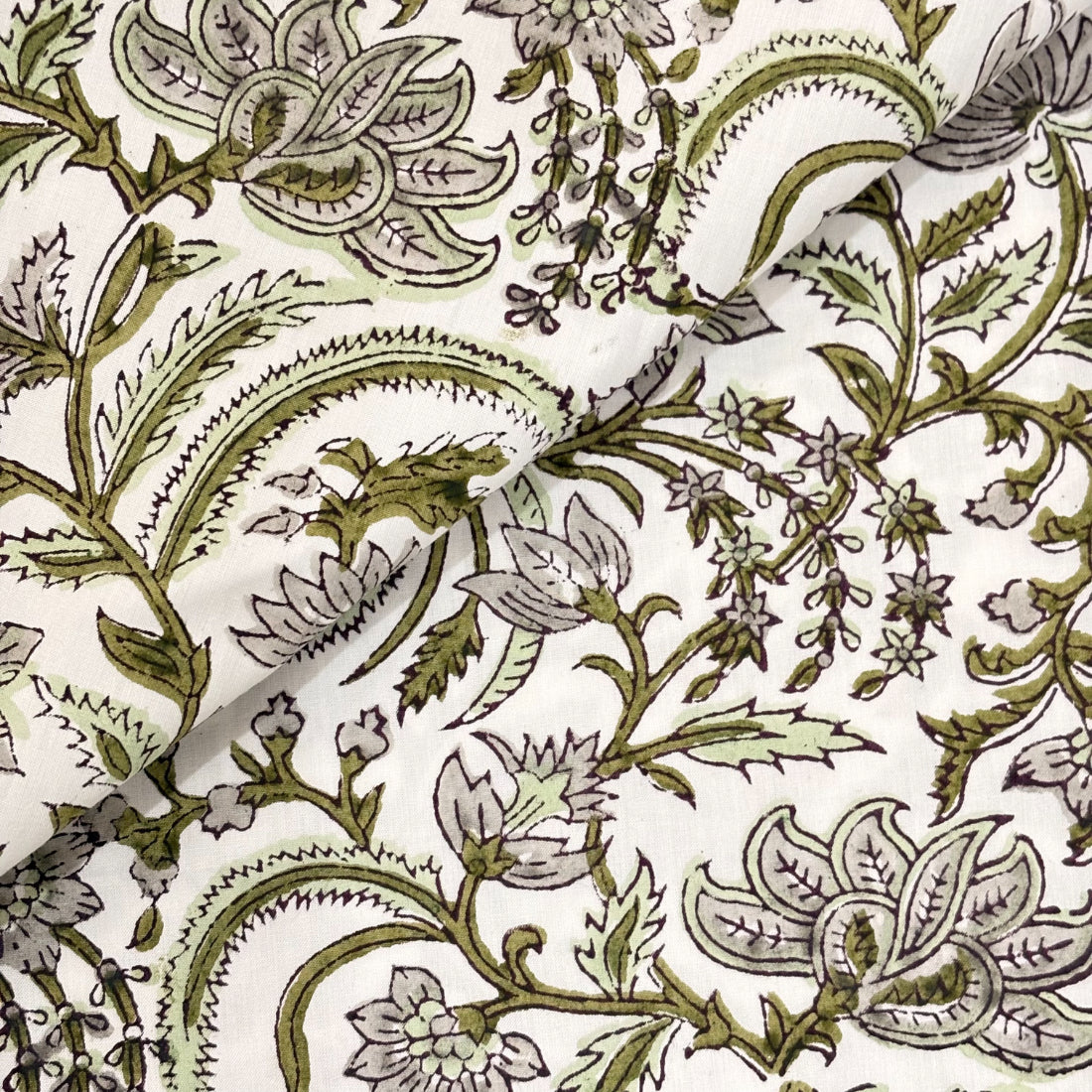 Close-up of a floral and leaf patterned fabric in green on a white background