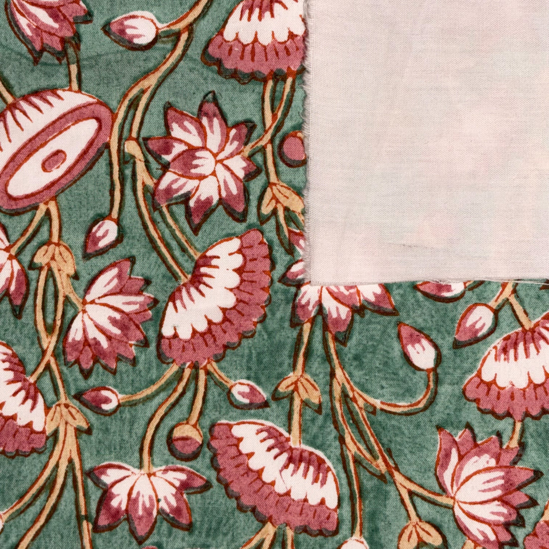 A close-up of a patterned textile or wallpaper corner showing a green background with pink and cream floral motifs and a plain light beige fabric section at the top right.