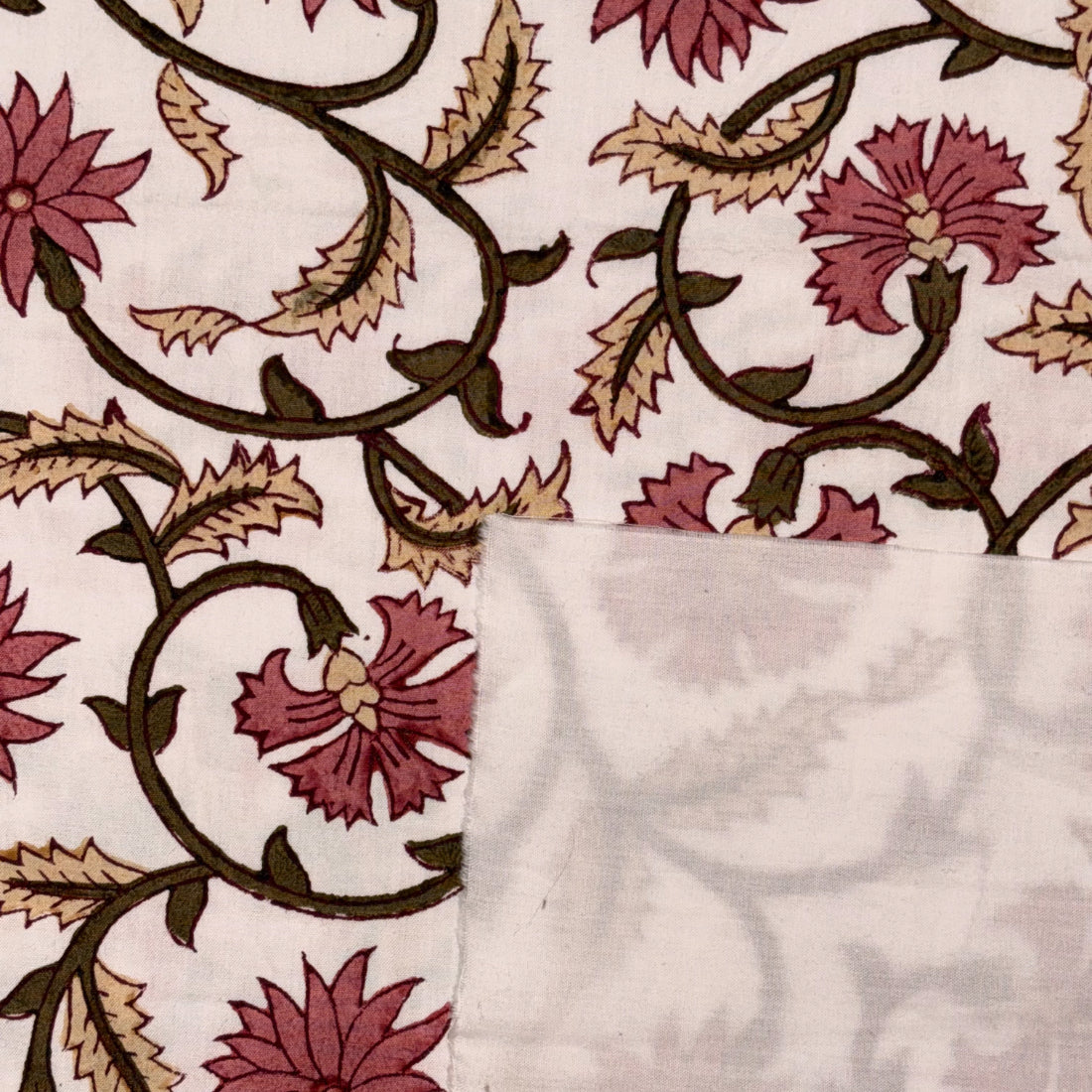 A close-up of a printed textile or fabric swatch with a cream background, dark brown vine and leaf motifs, and muted pink floral shapes. A folded section reveals the reverse side, which is a very light gray/off-white tone with a faint floral print.