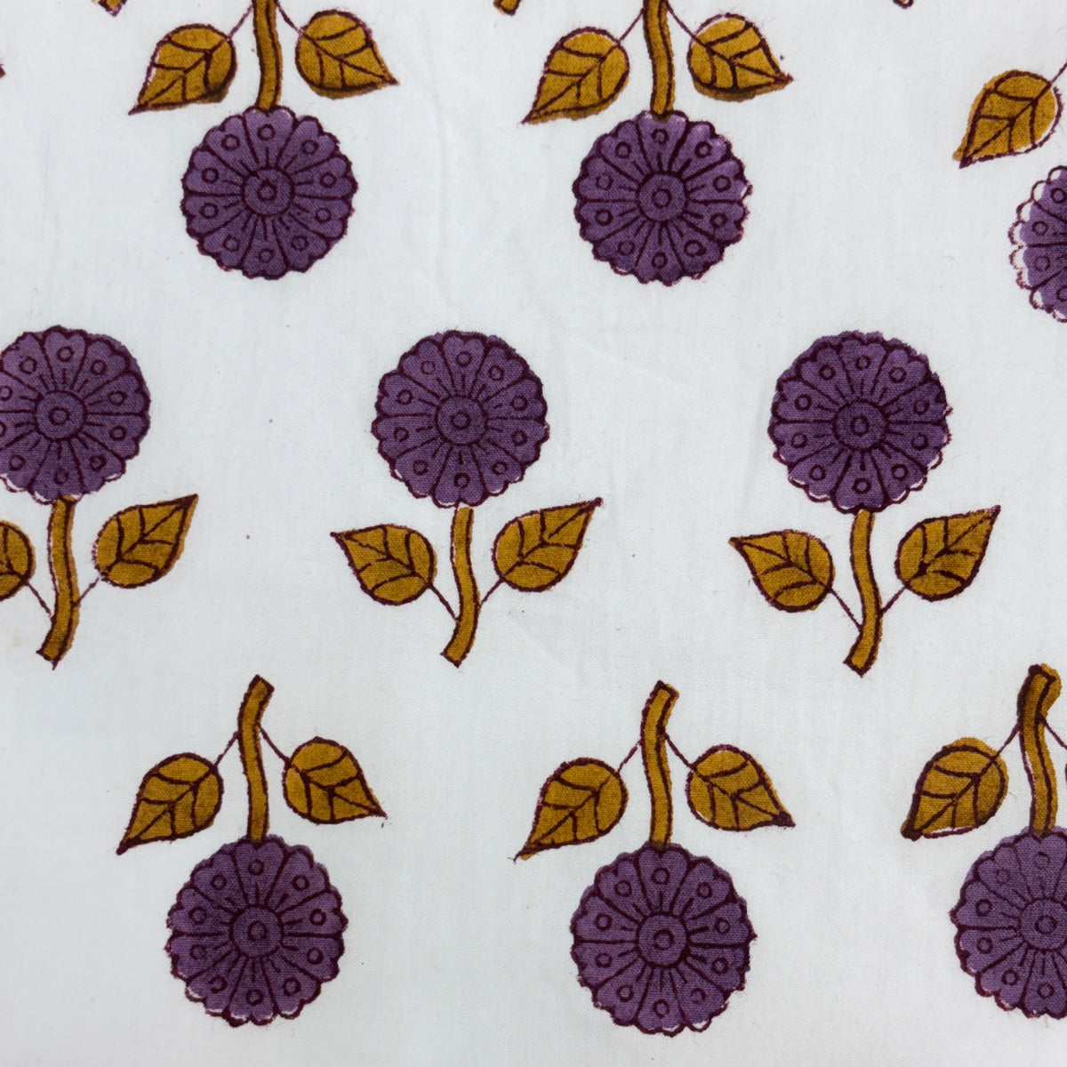 White fabric with a repeating block-print pattern of purple flowers and mustard yellow leaves.
