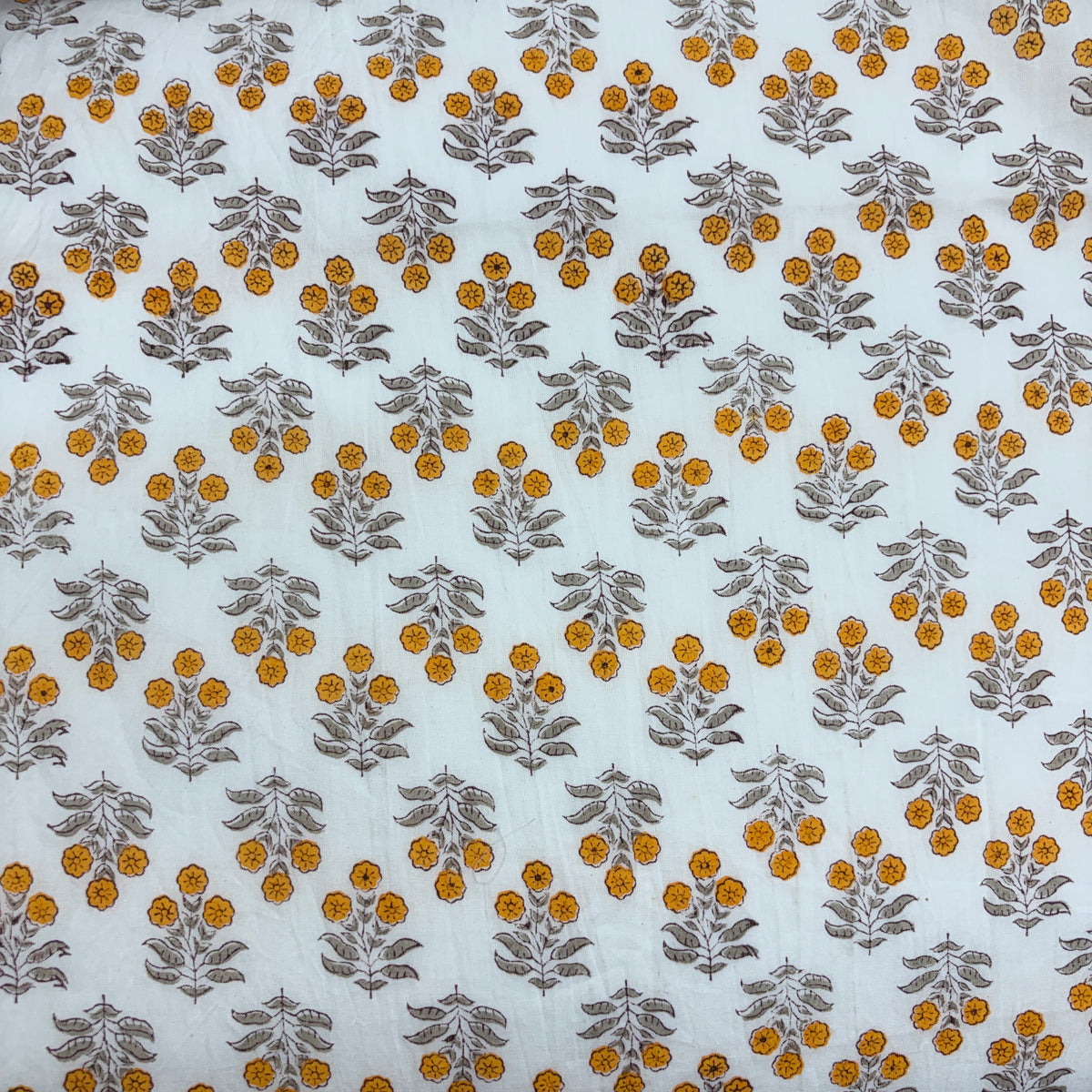 White fabric with a repeating block-printed pattern of mustard yellow flowers and gray-green leaves.