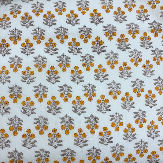 White fabric with a repeating block-printed pattern of mustard yellow flowers and gray-green leaves.