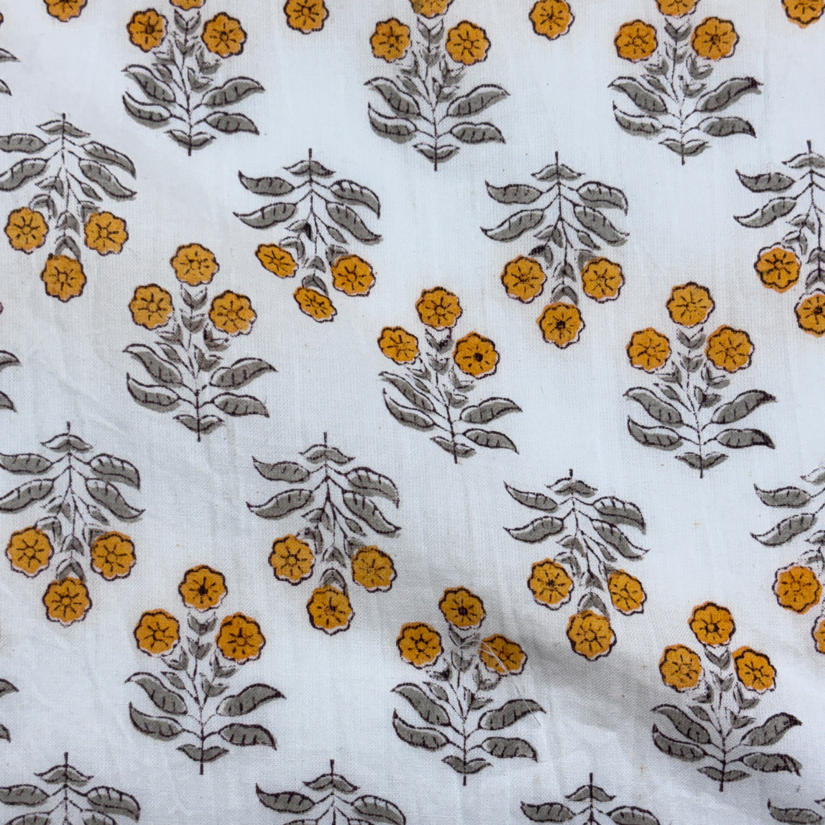 White fabric with a repeating block-print style floral pattern featuring mustard yellow flowers and gray-green leaves.