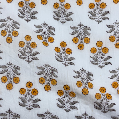 White fabric with a repeating block-print style floral pattern featuring mustard yellow flowers and gray-green leaves.