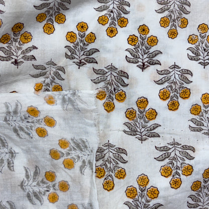 White cotton fabric with a block-printed floral pattern featuring mustard yellow flowers and gray-green leaves.