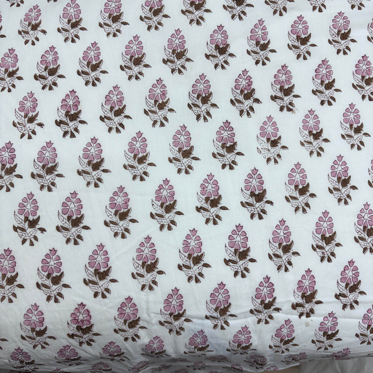 White cotton fabric with a repeating block-printed floral pattern in pink and brown.