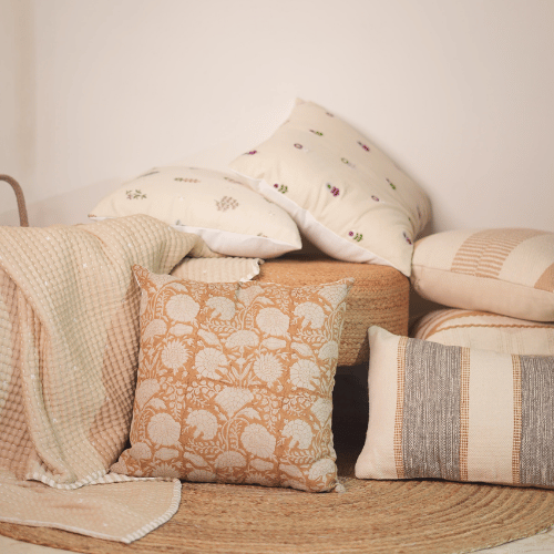 Collection of decorative pillows and a blanket on a wooden surface with a neutral background