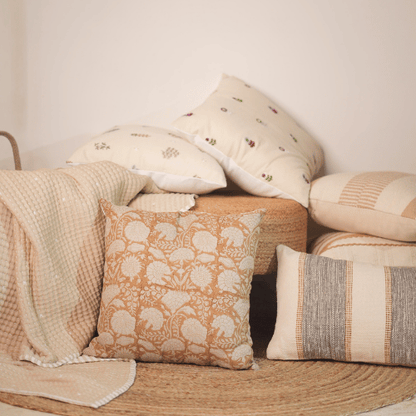 Collection of decorative pillows and a blanket on a wooden surface with a neutral background