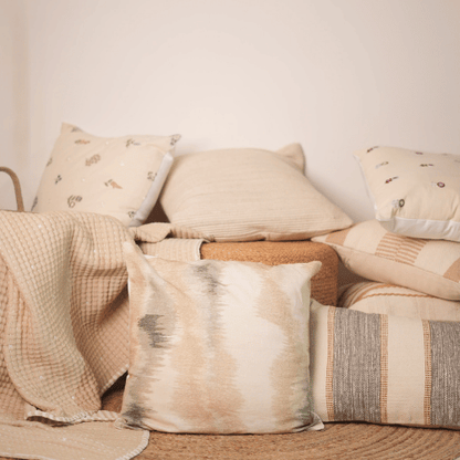 Collection of textured pillows and blankets on a sofa against a neutral wall.
