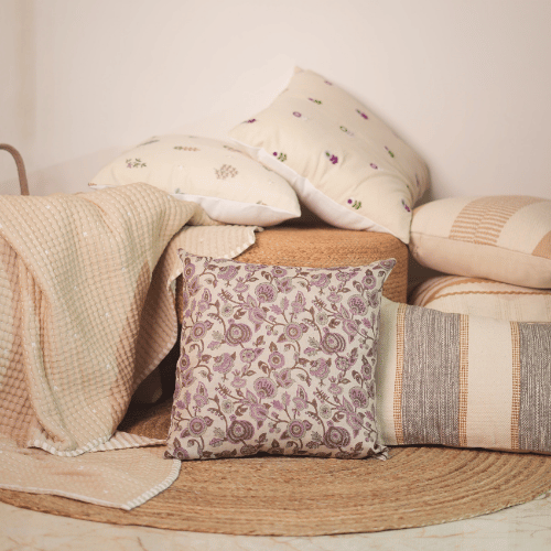 Decorative pillows and blankets on a woven surface with a neutral background