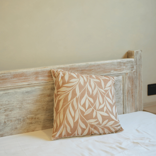 Decorative pillow with leaf pattern on a bed against a wooden headboard.