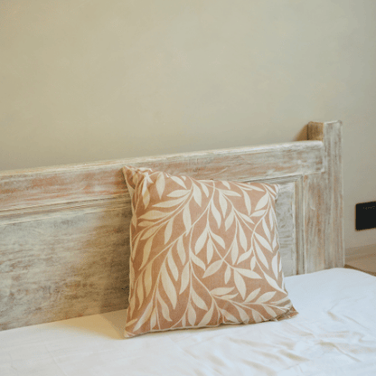 Decorative pillow with leaf pattern on a bed against a wooden headboard.