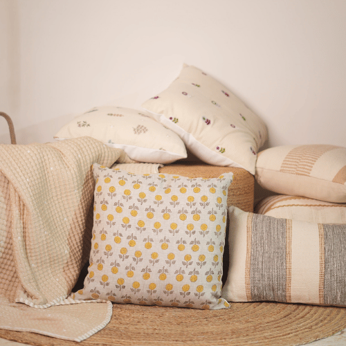 Collection of patterned pillows and a blanket on a wooden surface with a neutral background