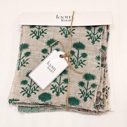 A folded linen fabric swatches set with a green botanical dandelion pattern on a beige background, packaged with a white header card and a white paper tag tied with twine.